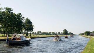 Kanaal met meerdere boten, omgeven door gras en bomen in een landelijk gebied.