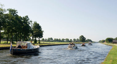 Kanaal met meerdere boten, omgeven door gras en bomen in een landelijk gebied.