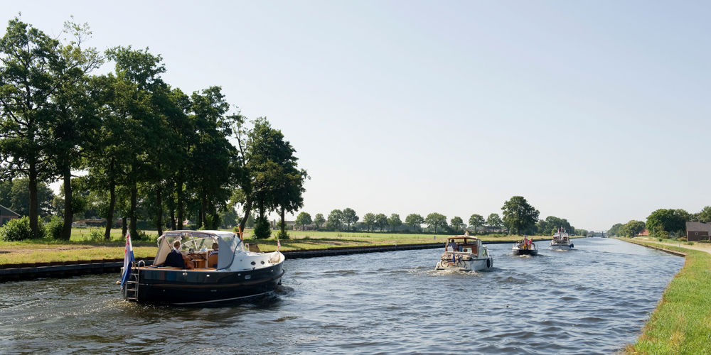 Kanaal met meerdere boten, omgeven door gras en bomen in een landelijk gebied.
