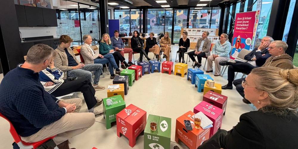 Mensen zitten in een kring in gesprek, met gekleurde SDG-blokken in het midden.