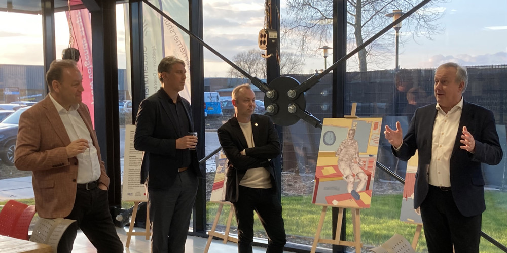 Vier personen in gesprek in een moderne ruimte met grote ramen en kunstwerken op ezels.